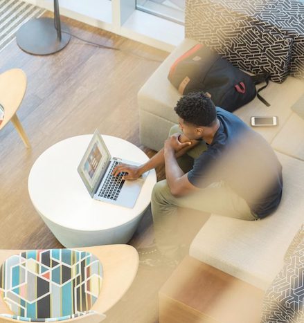 Overhead image of college student working at coffee table with laptop, phone and backpack